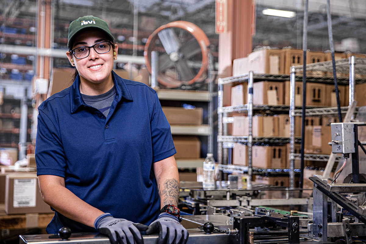 Female worker in a warehouse wearing a blue polo shirt, green cap, and gloves