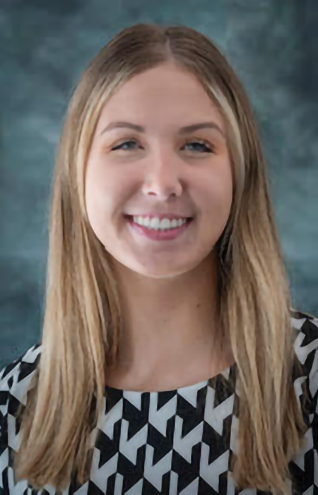Person with blonde, beyond shoulder-length hair wearing a patterned black and white dress shirt. 