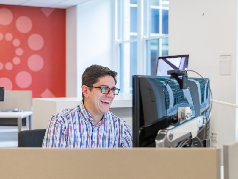 A worker sitting at his computer with a wide smile looking at his computer screen.