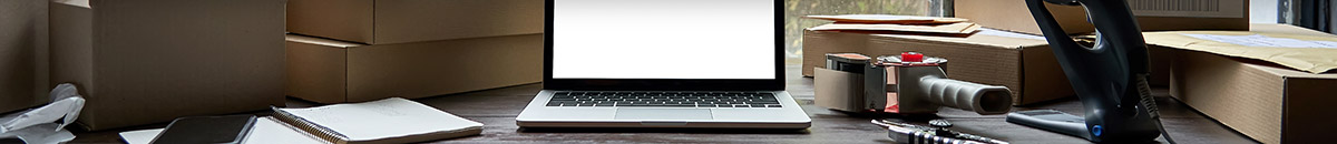 Desktop with laptop in the middle, and packing tape, papers and boxes surrounding it