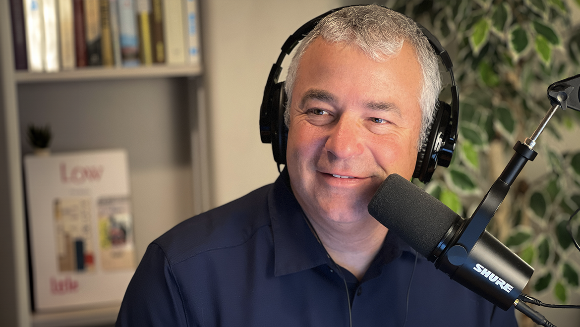 A white man with gray and white pair wearing a set of over the ears head phones with a large microphone close to him