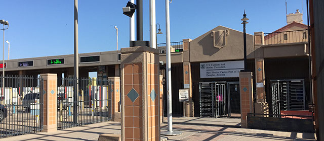 Red stone and stucco building entrance with a lamp post, and fencing with drive lanes on the left and a blue sky above