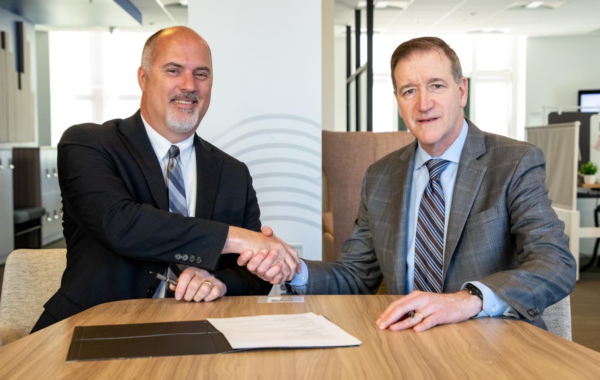 Two men shaking hands over a signed MOU