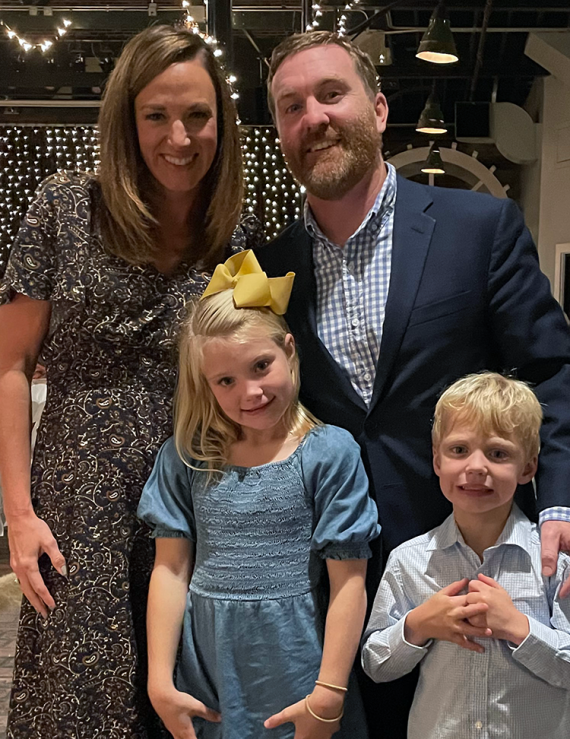 Two adults and two children in formal attire in an event space.