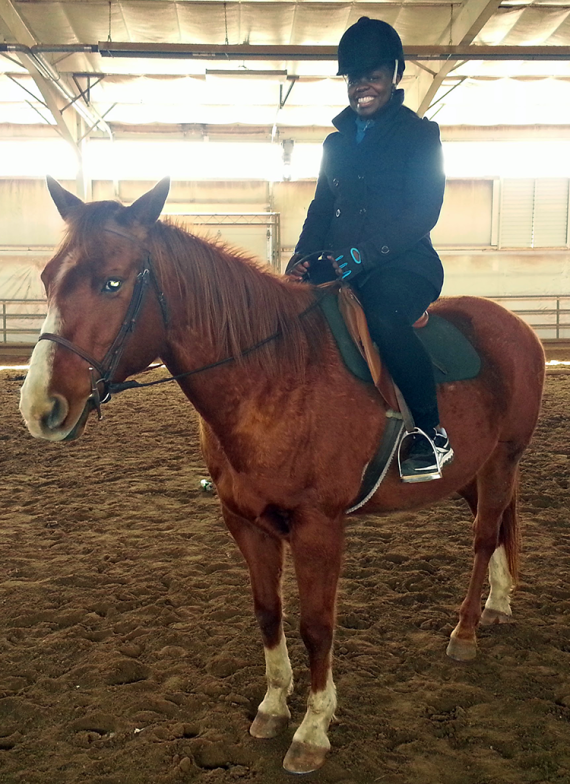 A person in a black jacket and black hat on a horse inside a building.
