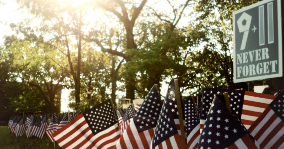Multiple small American flags stuck in grass in front of a sign saying