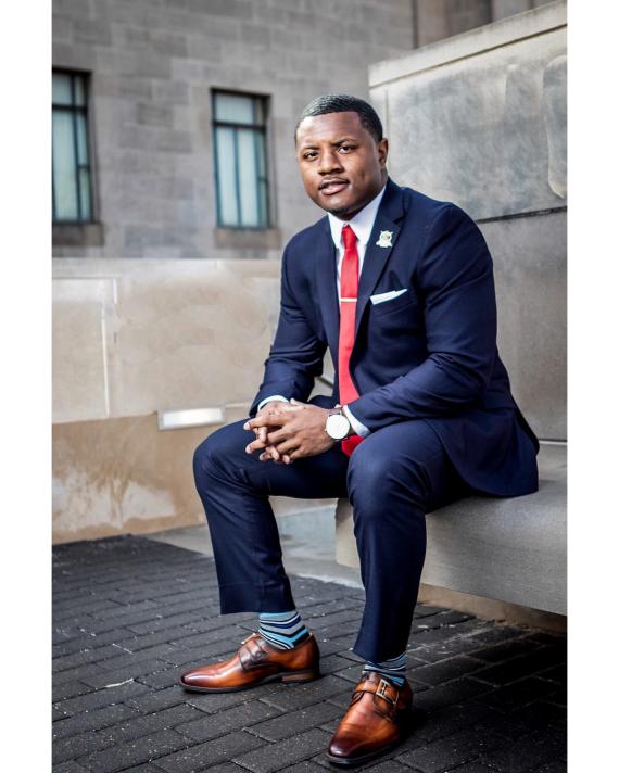 Man wearing a suit and tie sitting on a concrete bench outdoors.