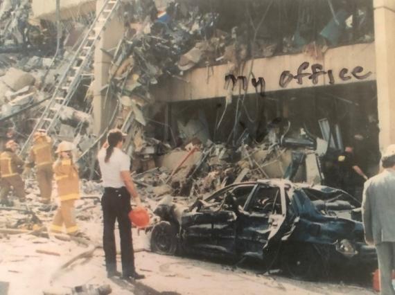 A man looks at the damaged Murrah Federal Building as firefighters walk by.