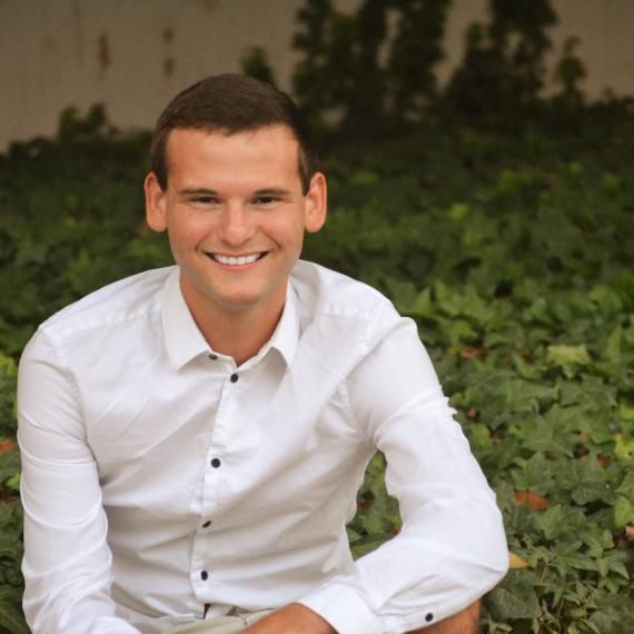 Jerry Tuttle, wearing a white button-down shirt, posing with his elbow on his knee. 
