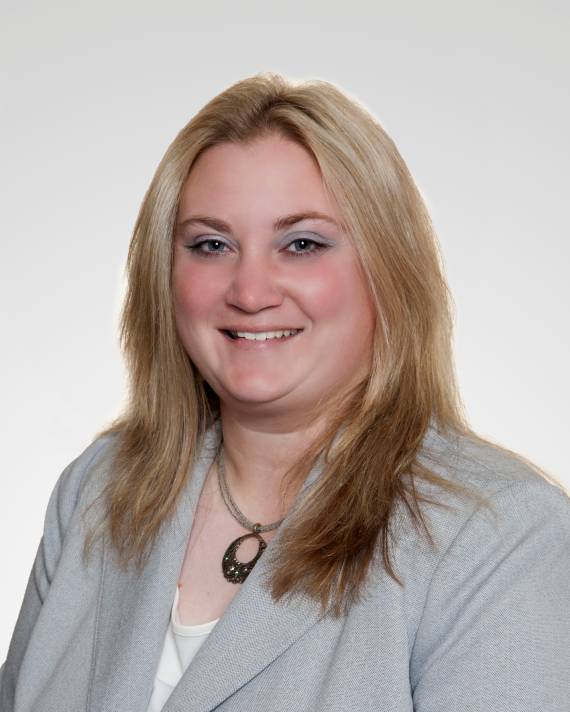 Woman wearing a suit jacket sits in front of a blank background.