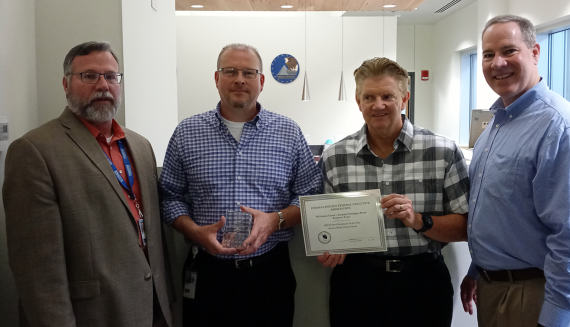 Terry Morgan, Jeff Warinski, Charles Woodring and Bill McGowan. Warinski holding glass trophy and Woodring holding certificate