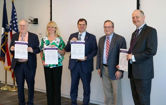 Five smiling people in business attire each holding a sheet of paper
