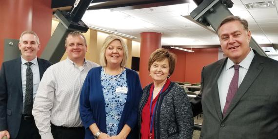 Five people posing for a photo in in front of the soon-to-be completed seismic renovation project.
