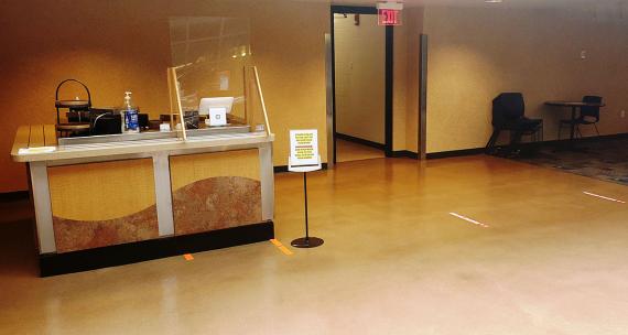 A small counter with a sneeze guard installed and a space cut out to pass a payment device through it.