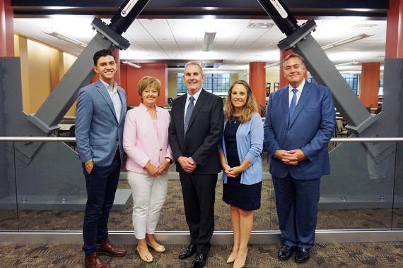 Five people stand in front of a viscous damper at a seismic renovation completion event.