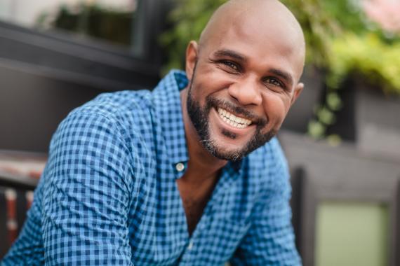 Steven Baugh - dark complexed, bald with full beard, smiling, wearing a blue plaid shirt. 