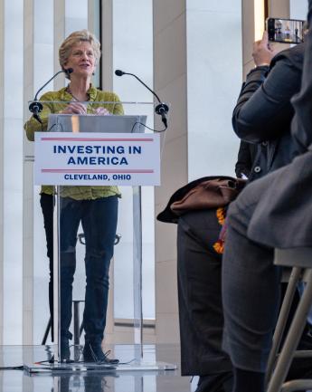 Medium shot of Administrator Carnahan at lectern with sign "Investing in America" talking to press at Stokes Courthouse
