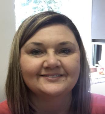A person smiling indoors wearing a pink top.