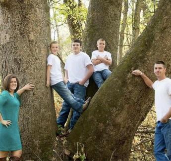 Five people standing outdoors smiling. Four are wearing jeans and white T-shirts and one is wearing a teal dress.