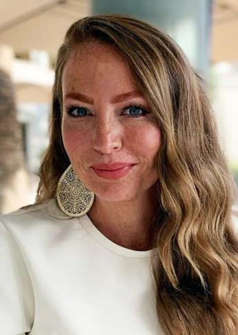 A person smiling and wearing a white shirt in an outdoor setting.