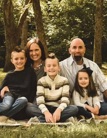Two adults and three children in a wooded outdoor setting