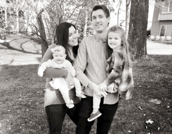 Two adults stand outdoors holding one child each.