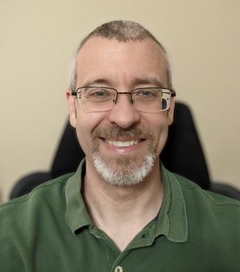 A headshot of Daniel Skelton, a man wearing glasses and a green collared shirt. 
