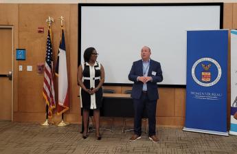 Two people in front of a room welcome a crowd to the event.