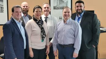 Six people wearing business attire standing in an office.
