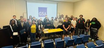 A group of about 30 people smile for a photo in front of a college classroom. 