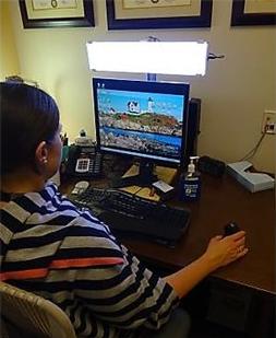 Photo of a woman working at a computer with a large lightbar above the monitor.