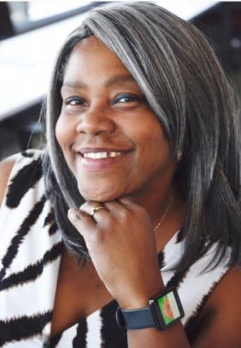 A head and shoulders photo of a woman with dark skin, eyes and hair wearing an animal print black-and-white top.