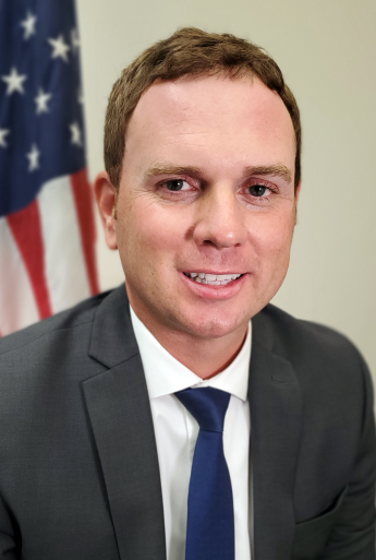 Person in suit and tie in front of an American flag.