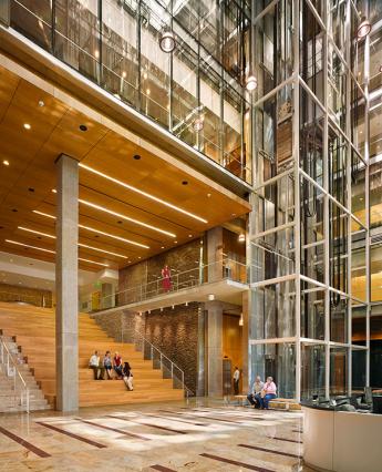 Interior atrium space with wood, lights and glass, with people sitting on benches