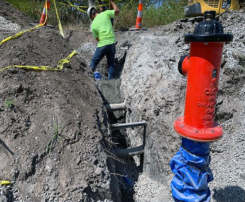 Man in hard hat with (backside view) digging a large trench with a new fire hydrant in the foreground.
