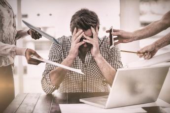 Man seated at computer with head in hands as too many people try to show him things