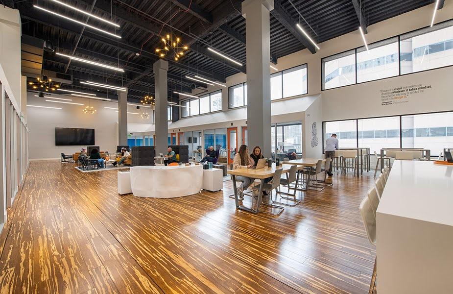 A large, open work space with a wood grain patterned floor; one wall has several windows, and quotations are printed on the wall.