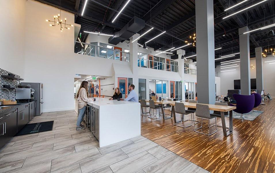 A tiled floor in the foreground of a large, open space with a kitchen and cupboards along one wall and a white bar with people standing.