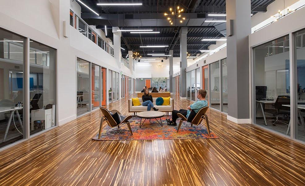 A large hallway with glass-walled offices and conference rooms with orange doors on either side.