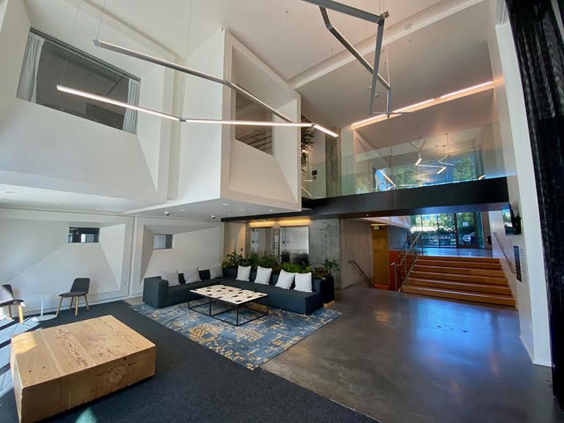 A large foyer with a staircase from one level to another and an L-shaped blue couch with coffee table; rugs and carpeting on floor.