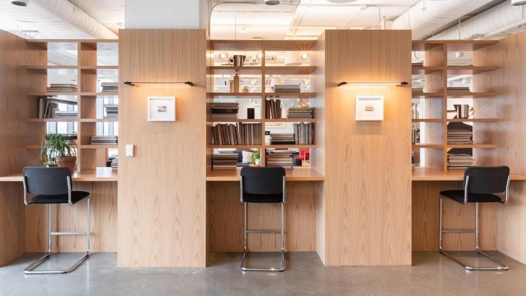 Three working booths with shelves at each booth with books, pitchers, and potted plants and small, framed artwork on the columns between.