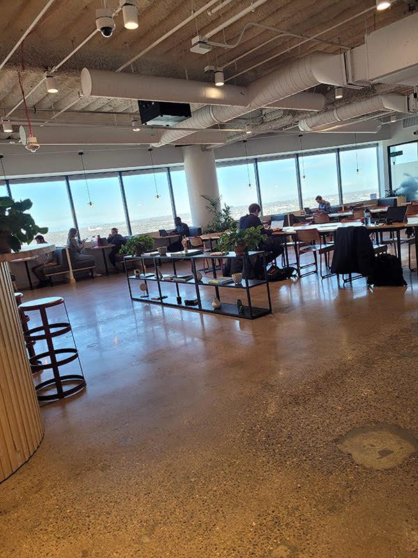Booths line one wall of an office space with a polished concrete floor, with windows along the far wall; opposite the booths are sofas.