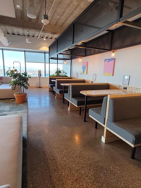 An open office space with a polished concrete floor and a bank of windows at the far end; there are several people sitting at booths