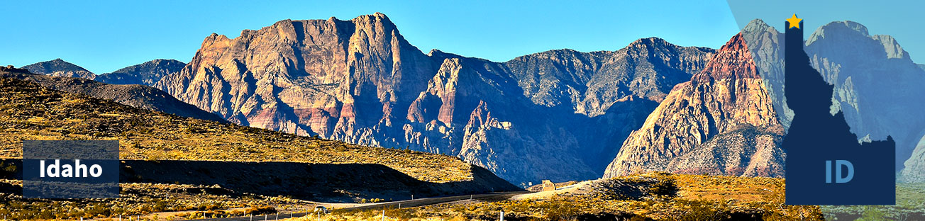 A road surrounded by golden grass on either side, and low rocky hills in the background and a blue sky, and the title Idaho at left and at right the state shape with a gold star at the north border